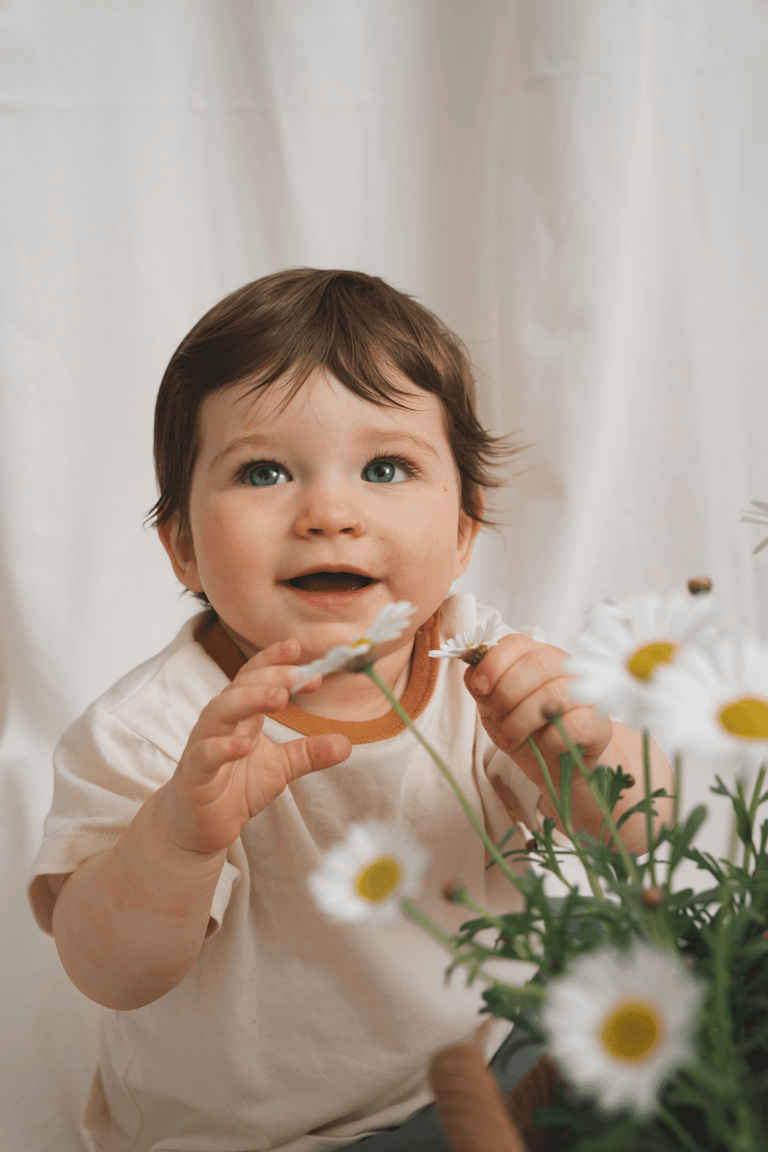Baby sitting in a studio setting touching flowers. Soft, textile background and soft studio light, editorial style edit.