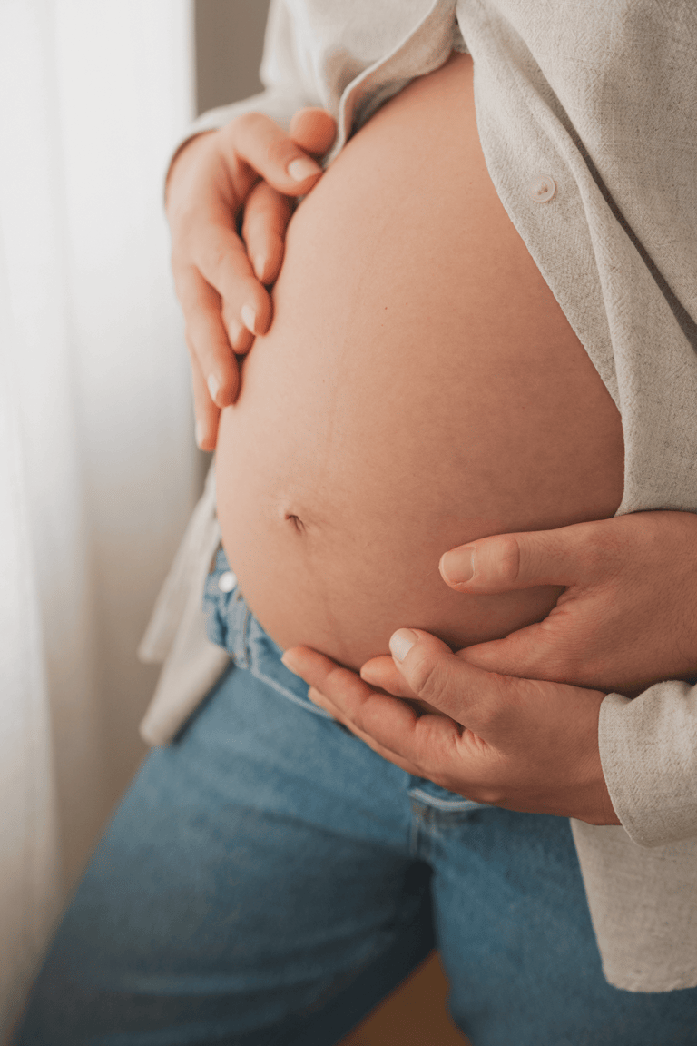 A closeup of a pregnant belly, man and woman holding hands on belly. Soft window light.