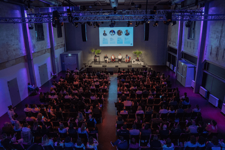 Indoor panel discussion in a blue lit conference space. Crowd sitting and listening.