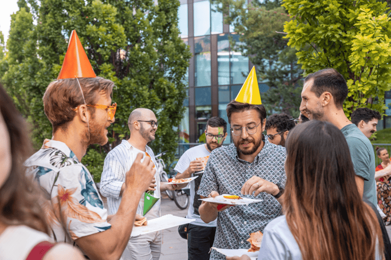 Group of people at an event wearing party hats outdoor, eating and chatting.