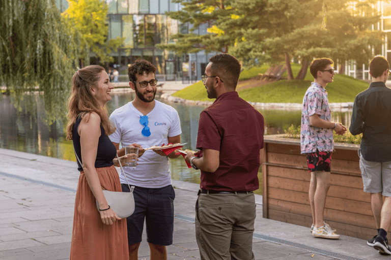 People talking and smiling at an event. Beautiful sunlight, location next to a pond surrounded by trees.