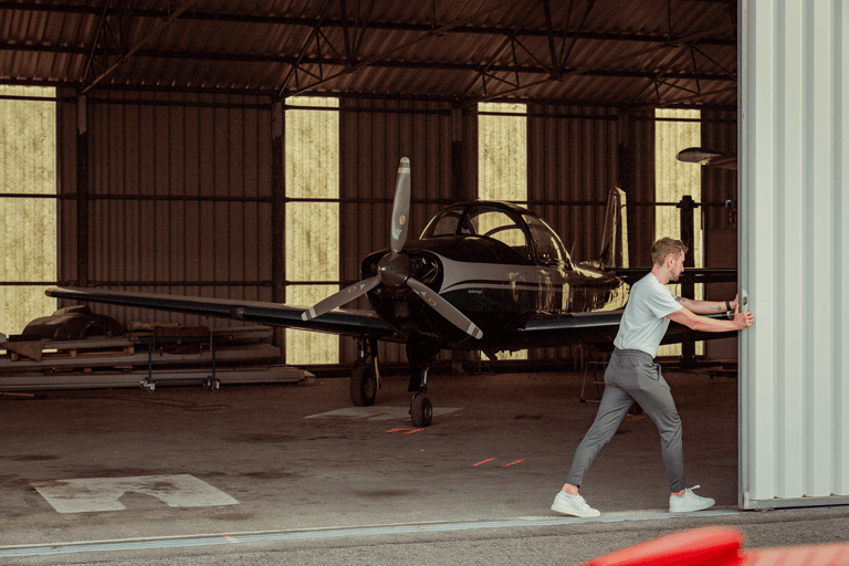 Young man pushing plane hangar door. Small private plane standing in the background.