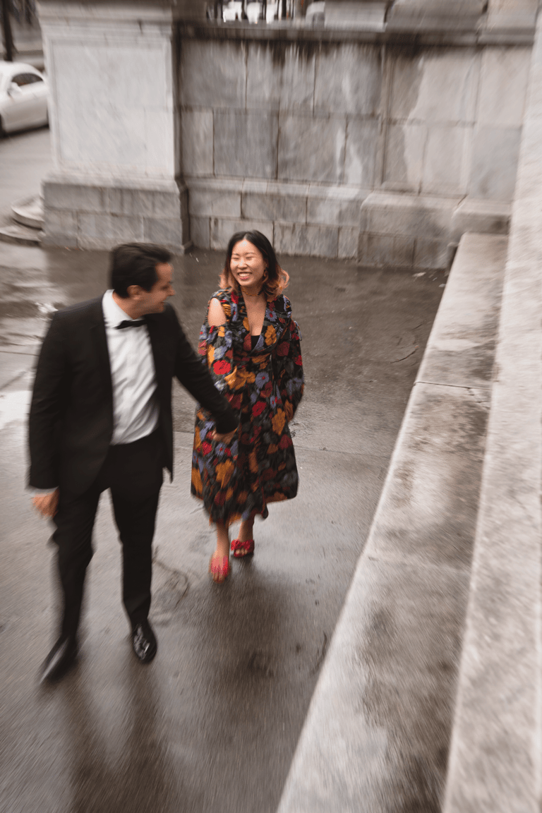 Long exposure shot of young couple dressed in festive clothes walking on the street smiling holding hands.