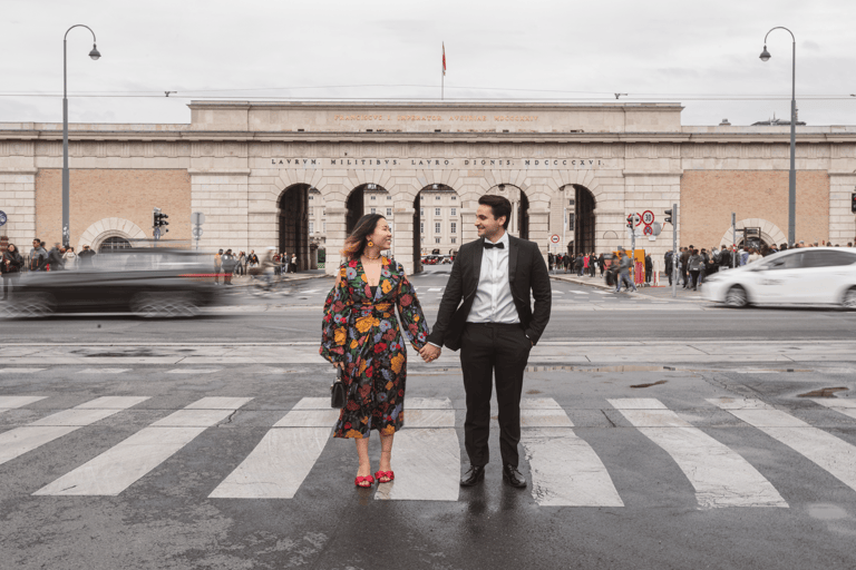 Festively dressed couple standing on a sidewalk in Vienna holding hands, car traffic behind them.