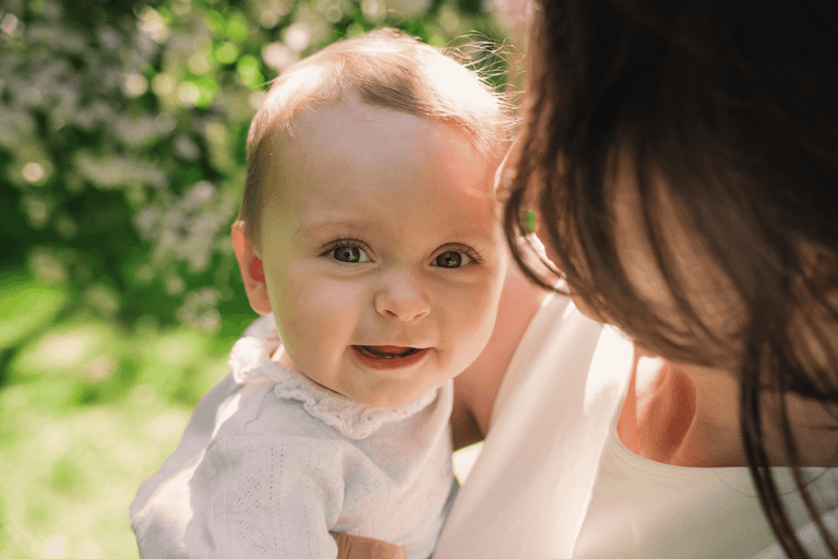 Portrait of baby looking into the camera in mom's arms. Beautiful portrait in the nature on a sunny day.