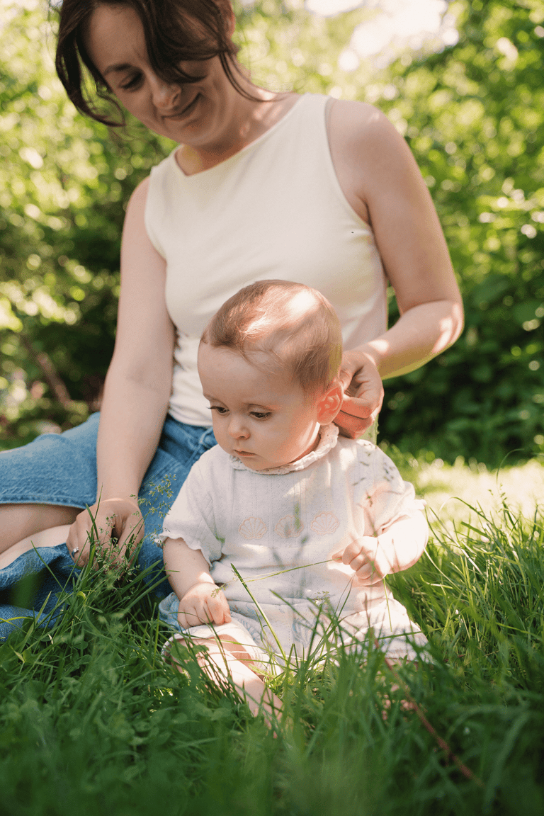 Mom and baby sitting on green grass in the nature. Sunny day.