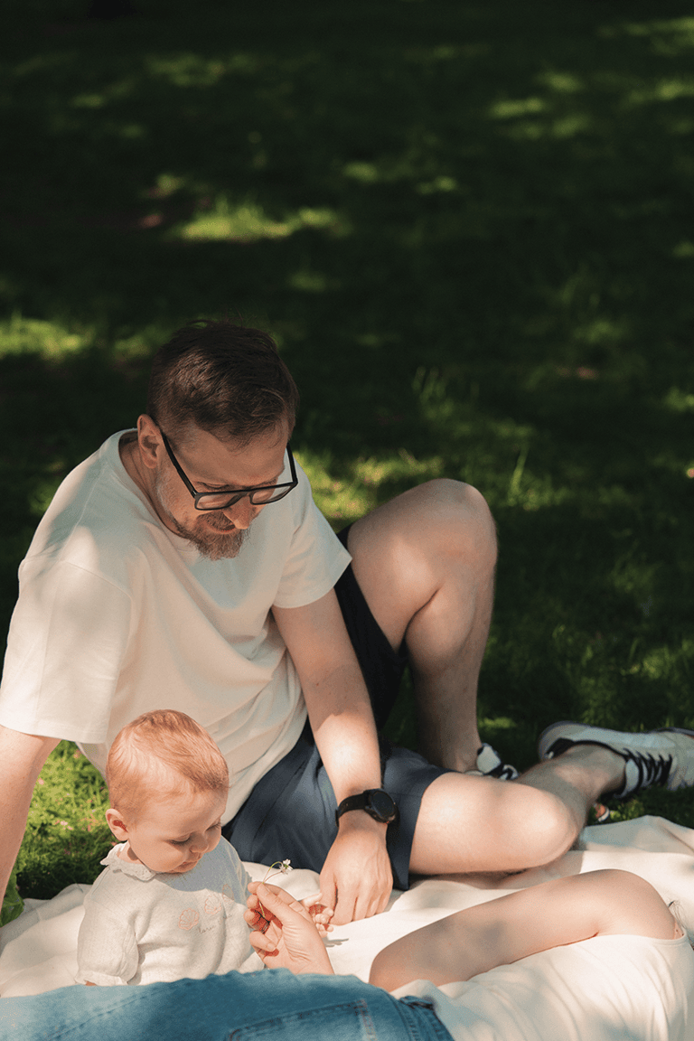Baby and dad on a picnic blanket on a sunny day.