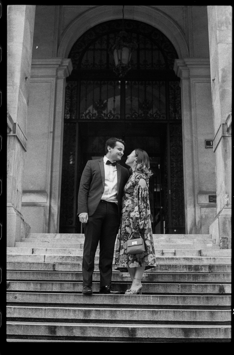 Couple in festive clothes standing on stairs in front of a historic building. Black and white film image.