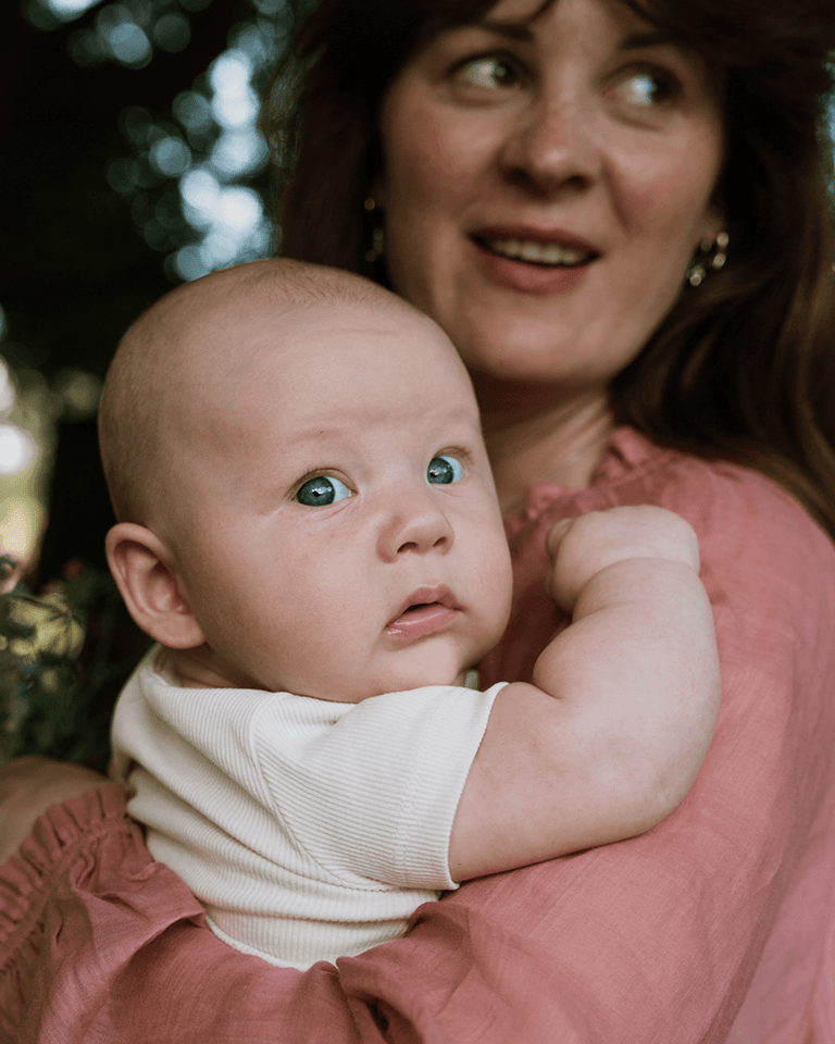 A close up shot of a baby face, being held by his mom. Mom's face visible in the background, blurred.
