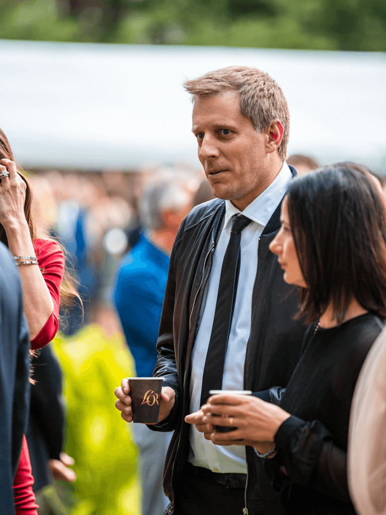 Lithuanian singer Saulius Prusaitis at an event outdoors with a coffee cup in his hand.