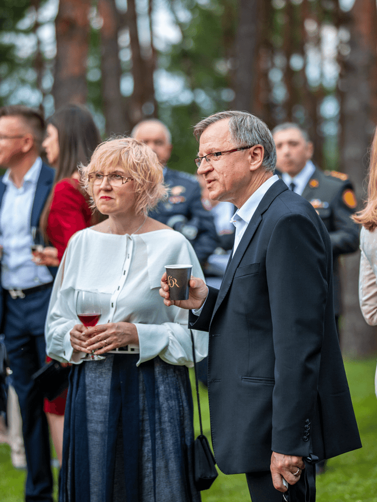 Middle aged man and woman standing at an outdoor event with drinks in their hands.
