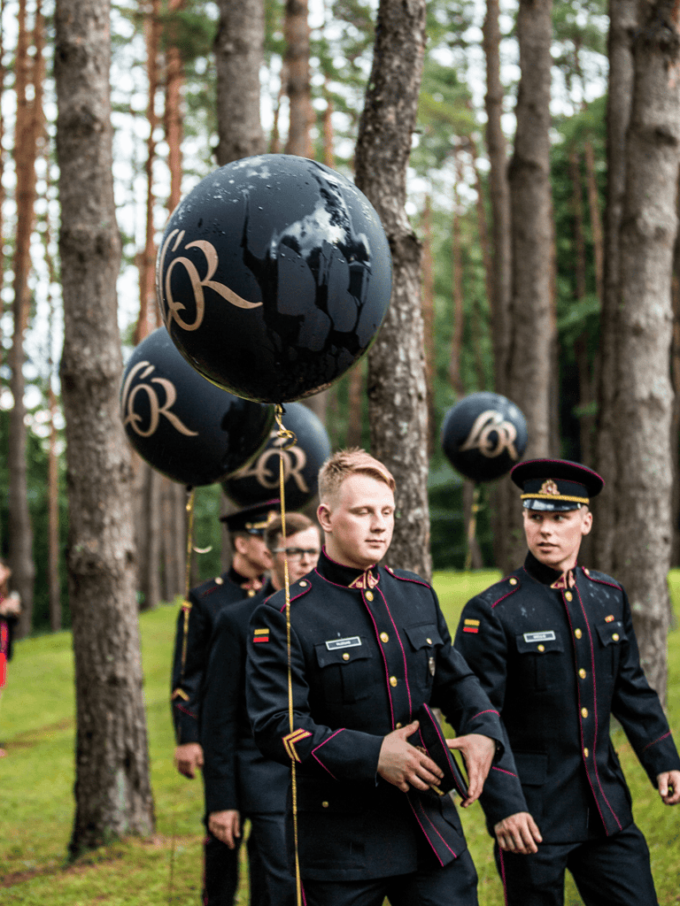 Officers waking in the forest with festive attire, black balloons around them.