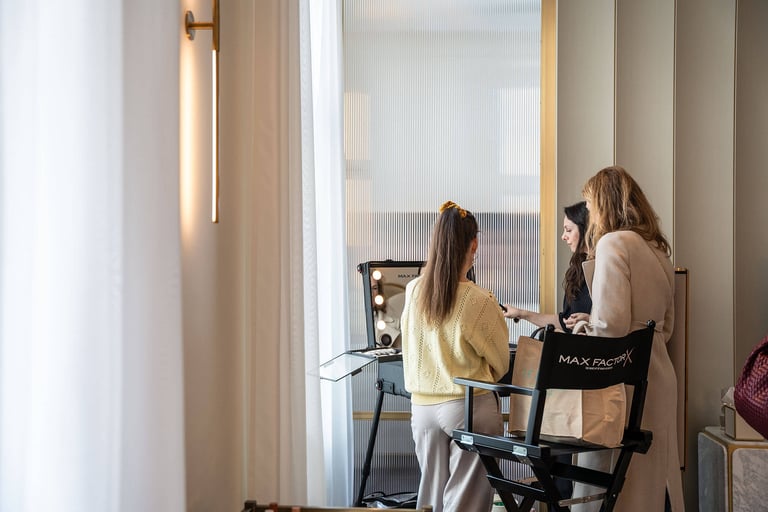 Three women standing next to a MaxFactor makeup station talking in a beautiful beige room.