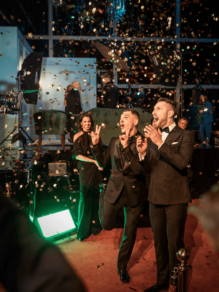 Two famous men at a red carpet event posing for a camera. Confetti flying in the air.