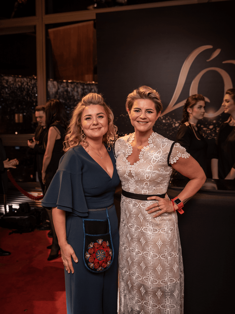Celebrity chef Beata Nicholson with her sister at a red carpet event posing in front of Lor coffee poster.