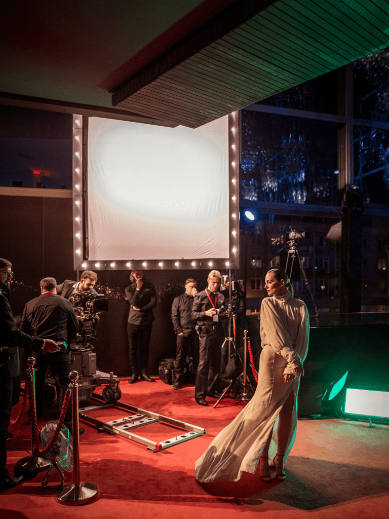 A woman celebrity with a beautiful dress at a red carpet event posing for a video camera in front of bright lights.