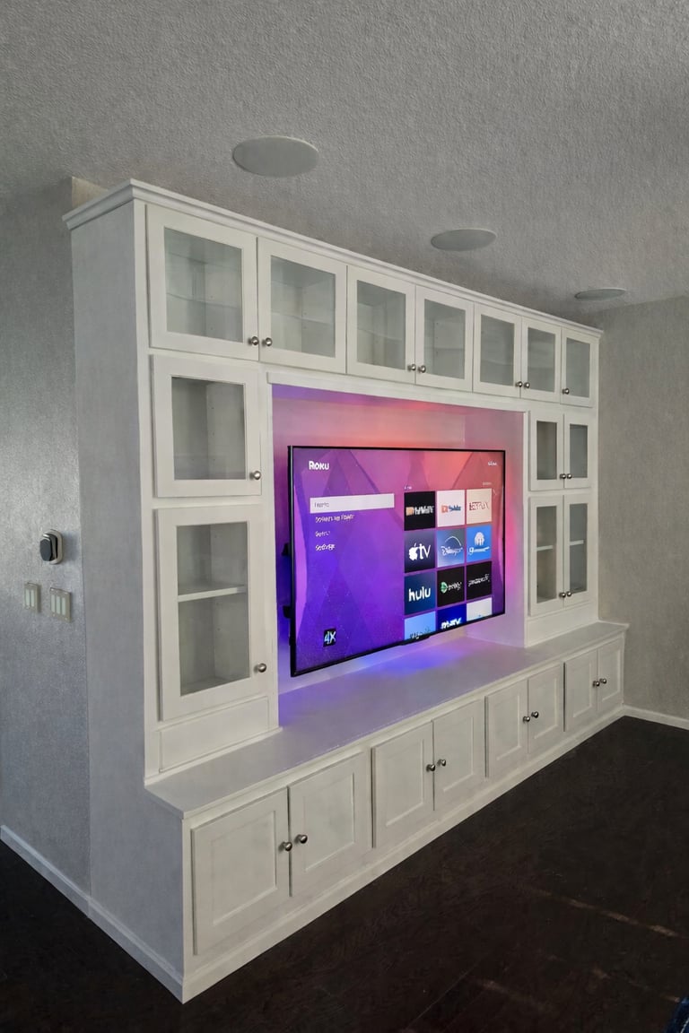 Custom white built-in entertainment center with glass cabinets and backlighting for a large Roku TV.