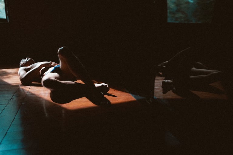 Photo boudoir homme nu en studio, lumière tamisée — Belle Tronche Montréal - Allongé sur parquet, intérieur sombre