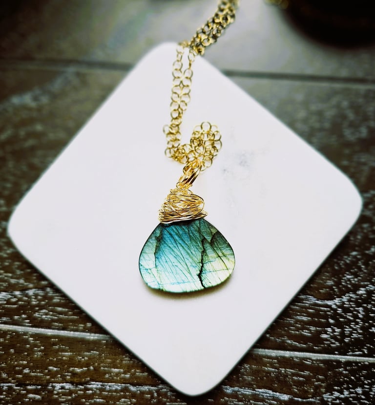 Handcrafted labradorite pendant with iridescent blue-green hues, wire-wrapped in gold, hangs on a delicate gold chain.