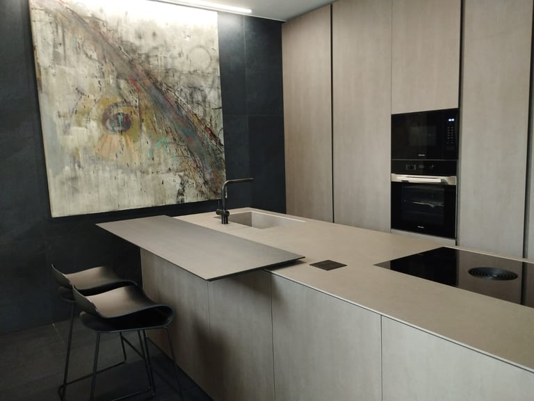 Modern minimalist kitchen featuring a concrete island, black bar stools, and abstract wall art.