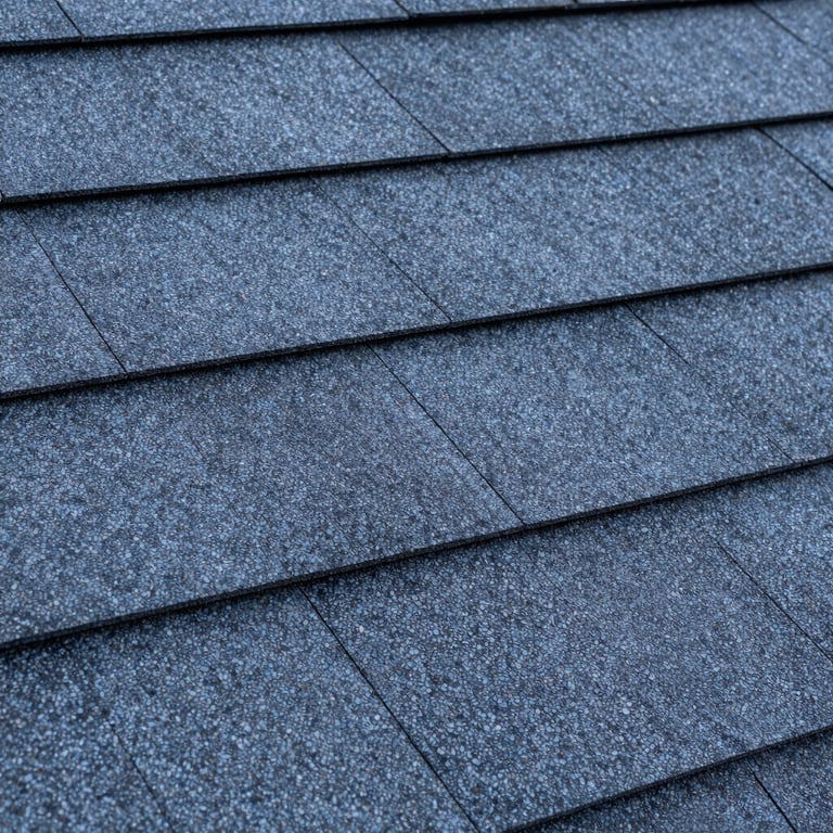 A close-up of high-quality, dark blue and grey architectural roofing shingles. Clean, professional North American / US construction material shot.