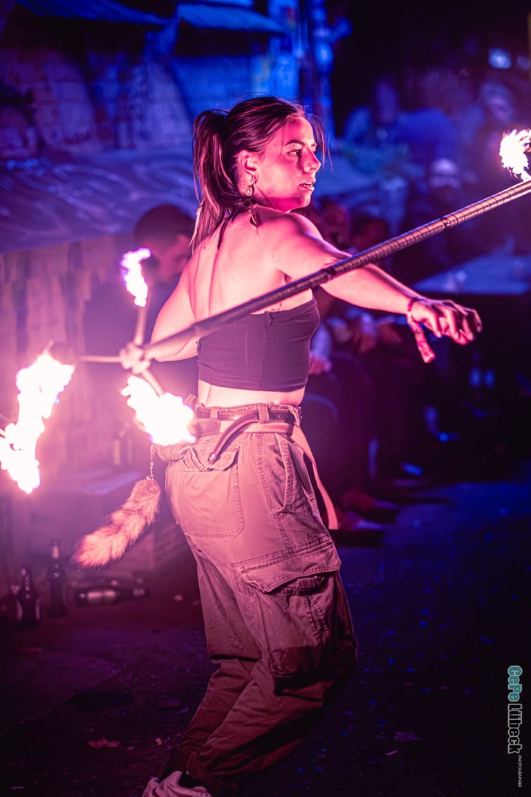 Female fire dancer performing a professional fire spinning routine with a lit staff at night.