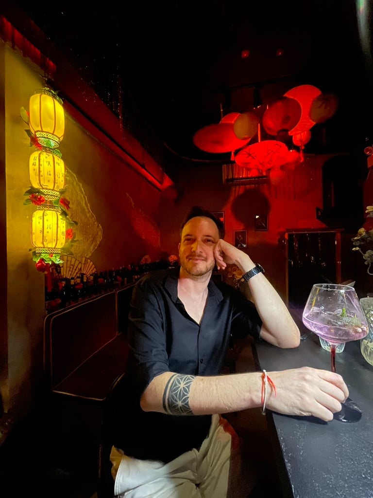 Unicris enjoying a cocktail at a dimly lit bar with red and yellow Chinese lanterns.