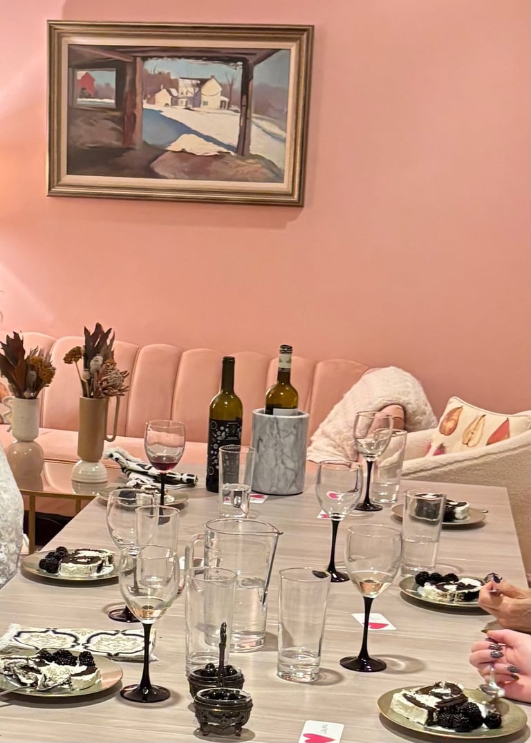 Elegant dinner table setting with wine bottles, desserts, and glasses in a pink room.
