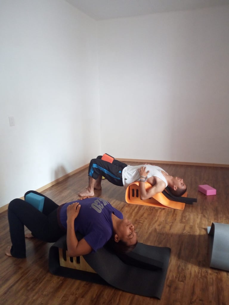 Dos personas realizando posturas de yoga restaurativo con extensiones de espalda, utilizando arcos