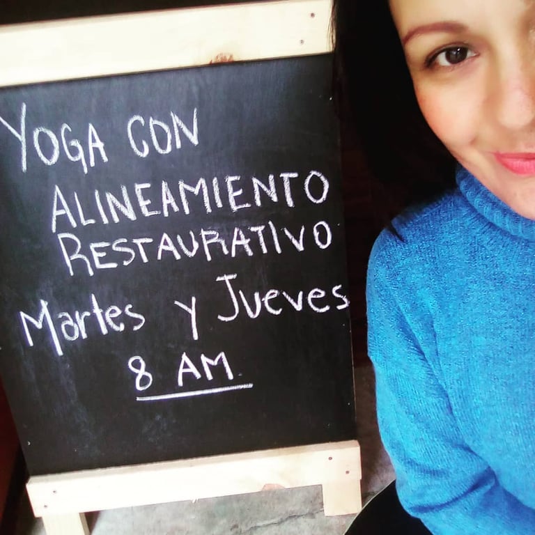 Mujer junto a una pizarra que anuncia Yoga con Alineamiento Restaurativo Martes y Jueves en Oaxaca