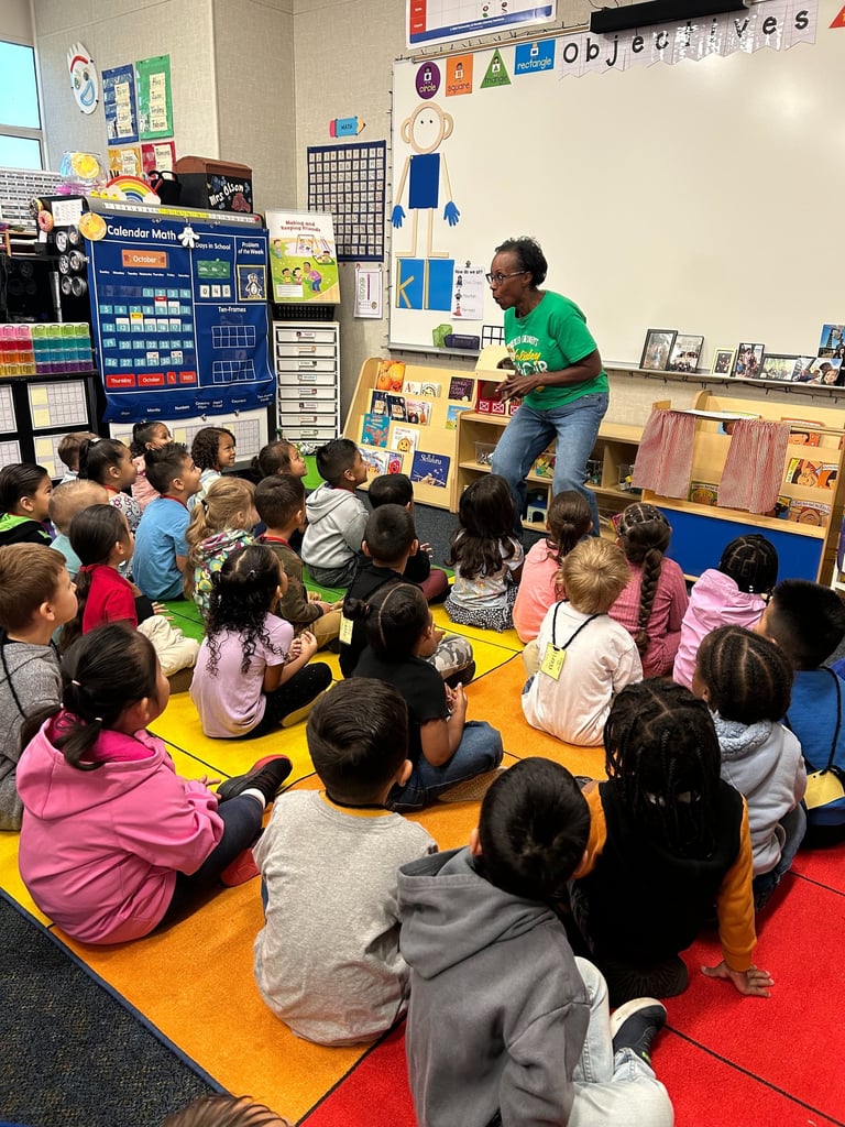 Music teacher leading a song with students sitting in a colorful classroom rug.