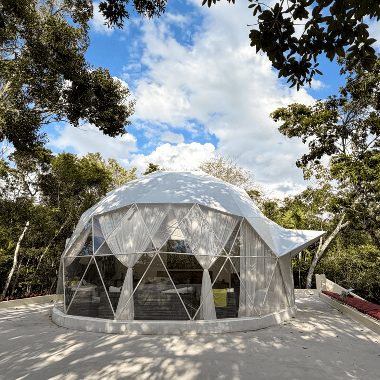 A luxurious white geodesic dome, Venamarte Glamping, nestled in the Mayan Jungle under a blue sky.