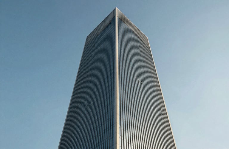 A low-angle shot of a glass and steel corporate tower in a Middle Eastern / Gulf financial district, reflecting the Oceanic Blue sky. Clean, minimalist composition.