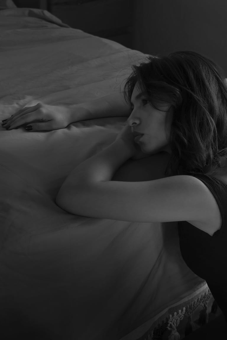 Retrato en blanco y negro de una mujer pensativa apoyando la cabeza en una cama