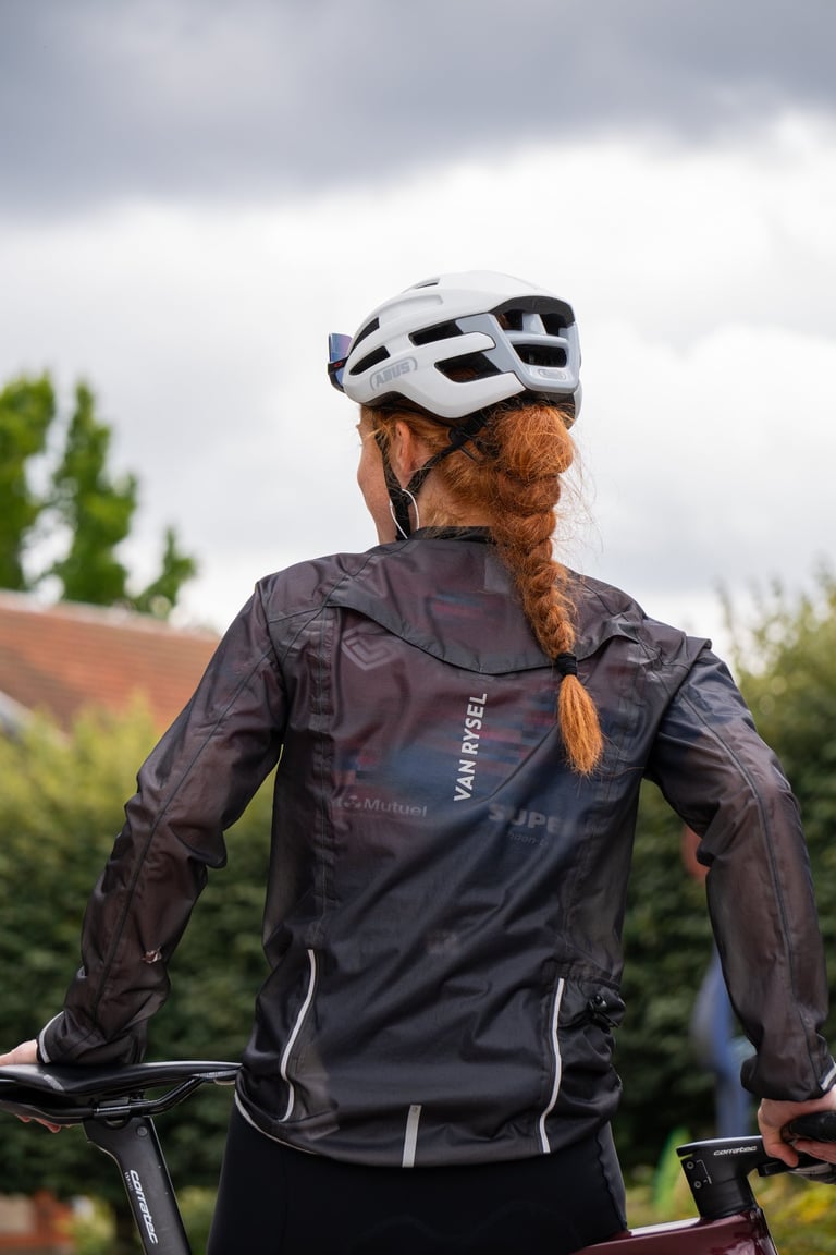 A female cyclist wearing a Van Rysel rain jacket and white Abus helmet standing with her bike.