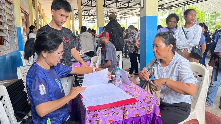 A woman signs official documents at a community registration table during a busy local event.