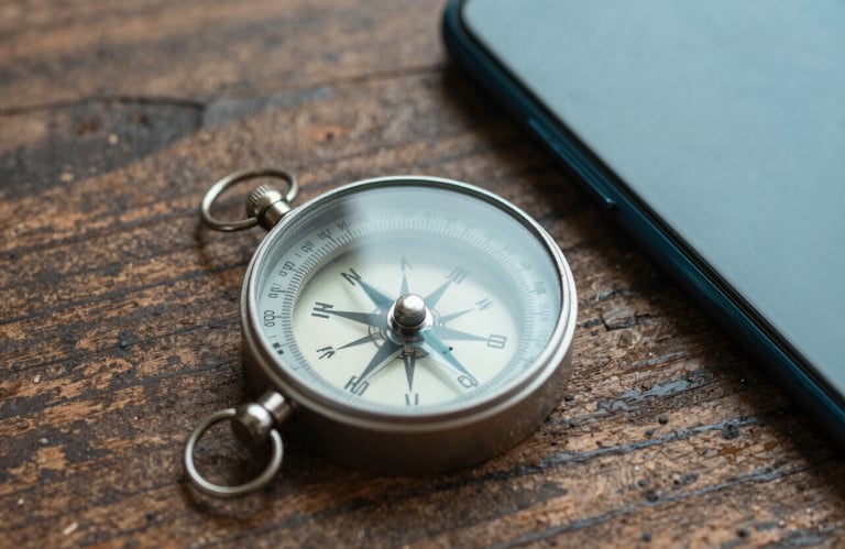 A macro shot of a compass and a smartphone lying on a rough wooden table, blending traditional travel with modern technology. Colors feature deep teal and off-white.