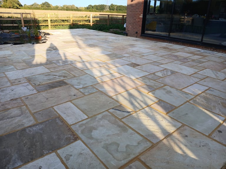 Modern garden patio featuring multi-tonal Indian sandstone paving slabs and a backyard pond.