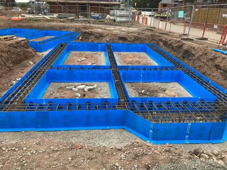 Reinforced steel rebar and blue formwork for concrete house foundations at a construction site.