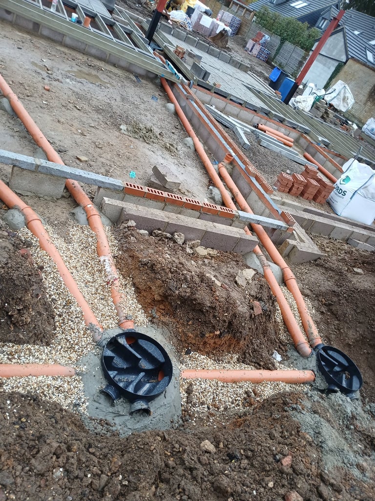 Underground drainage system installation with orange PVC pipes and inspection chambers on a house construction site.