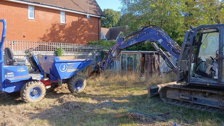 A blue mini excavator loading soil into a site dumper on a residential garden construction site.