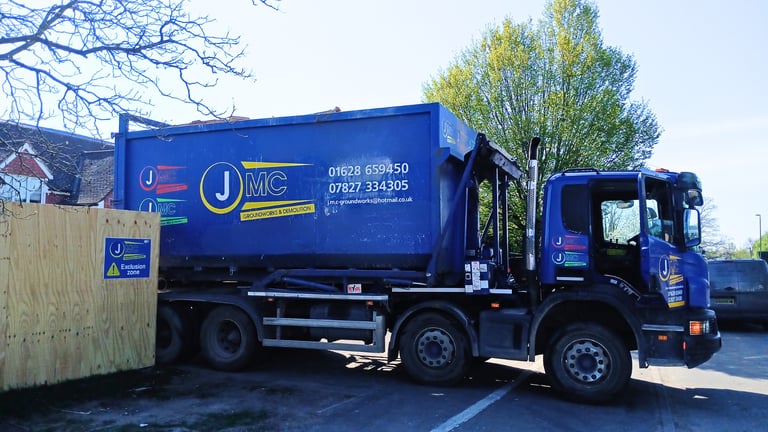 A blue JMC Groundworks and Demolition skip loader truck parked at a construction site.