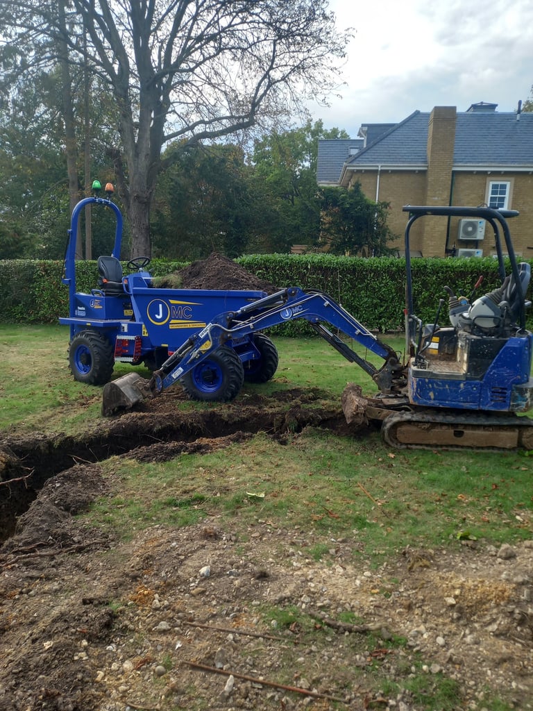 A blue micro excavator and tracked dumper digging a narrow trench for garden landscaping and groundworks.