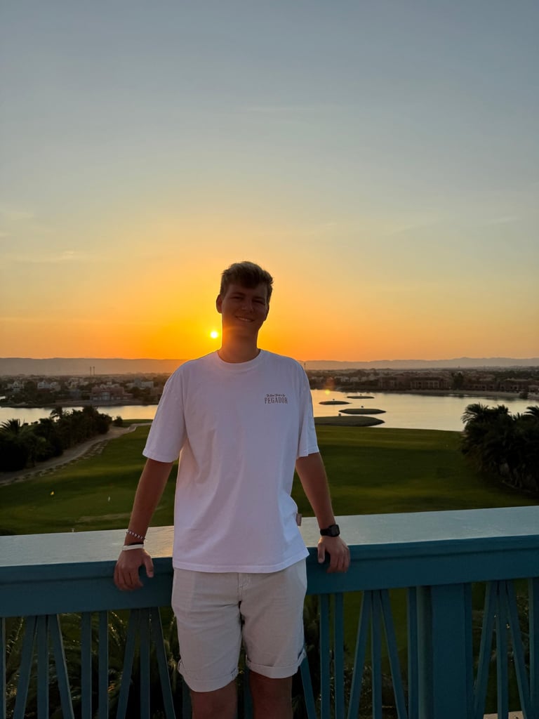 Ein lächelnder junger Mann in einem weißen T-Shirt steht auf einem Balkon, während über einem maleri