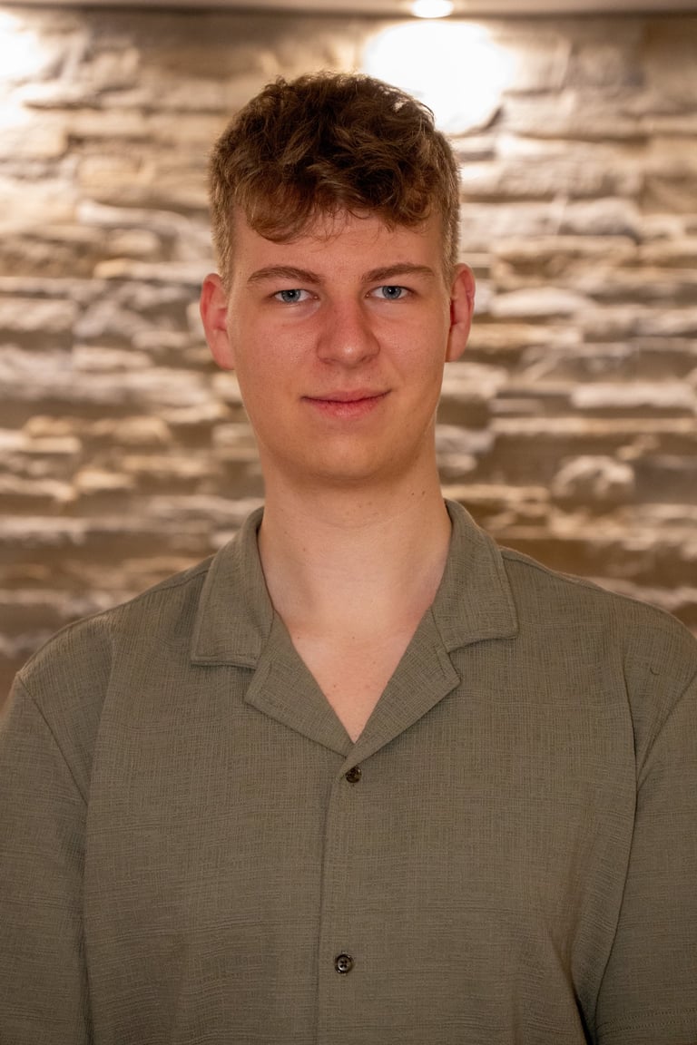 Porträt eines jungen Mannes mit blonden Haaren in einem grünen Hemd vor einer Steinmauer.