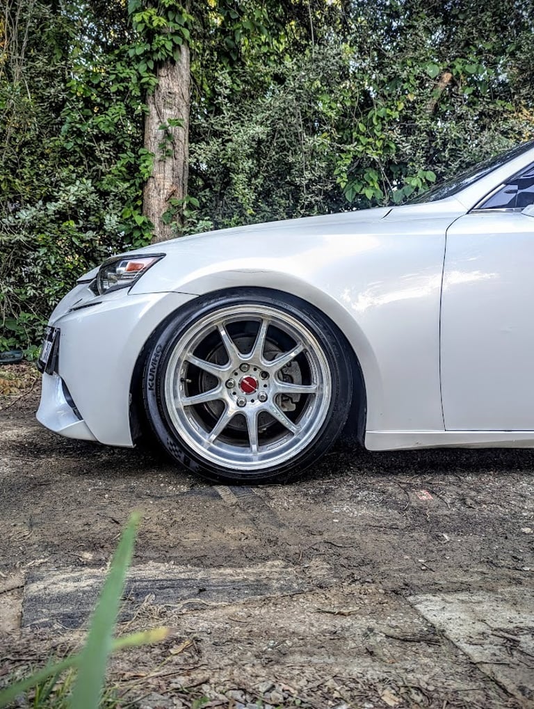 White luxury sedan featuring aftermarket chrome alloy wheels and lowered suspension parked on dirt.