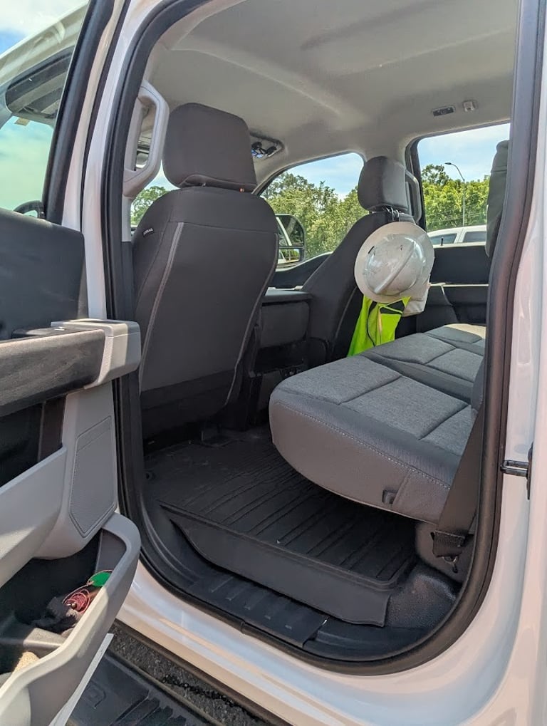 Interior view of a white pickup truck back seat with a hard hat and safety vest for construction work.