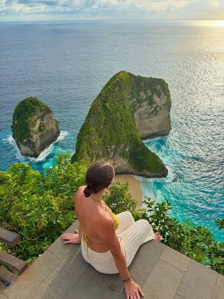 A woman looks over Kelingking Beach in Nusa Penida, Bali, featuring the iconic T-Rex shaped cliff.