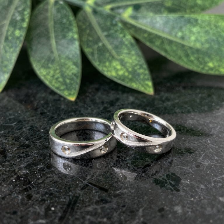 Close-up of a handcrafted silver ring with a subtle jade green accent, resting on a smooth gray stone.