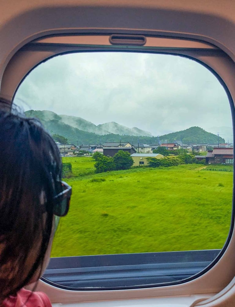 View from the Hikari Shinkansen window showing misty countryside and green fields on the journey to Kyoto, Japan.